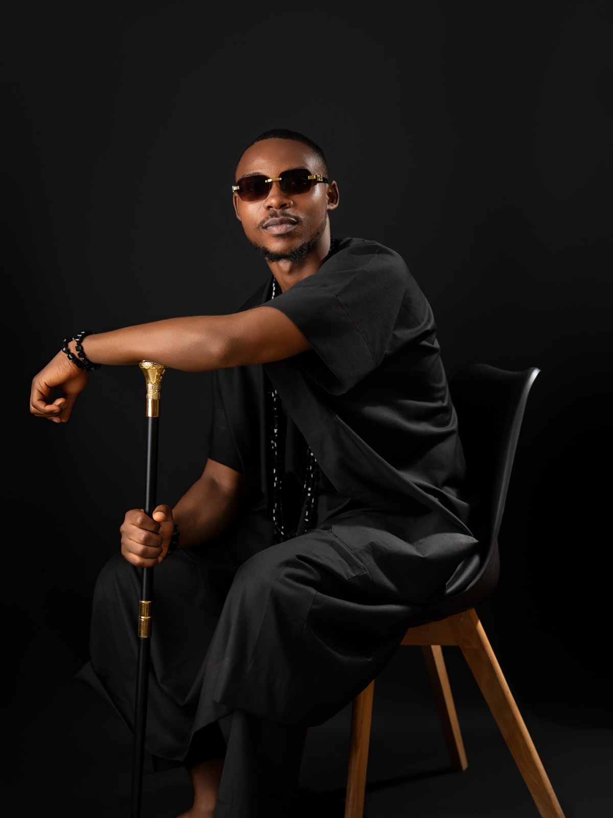 Man in sunglasses seated with a cane, low-key lighting