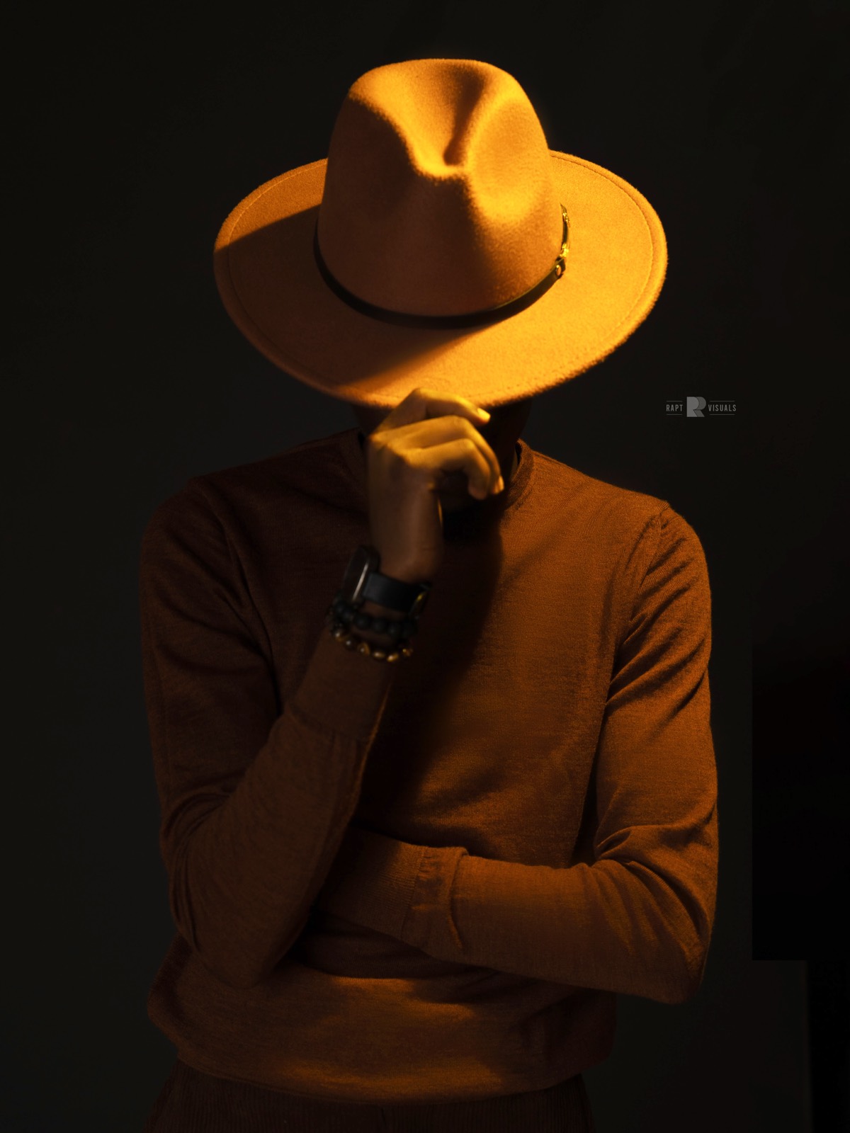 Portrait of a man in a rust hat, lit against a dark backdrop